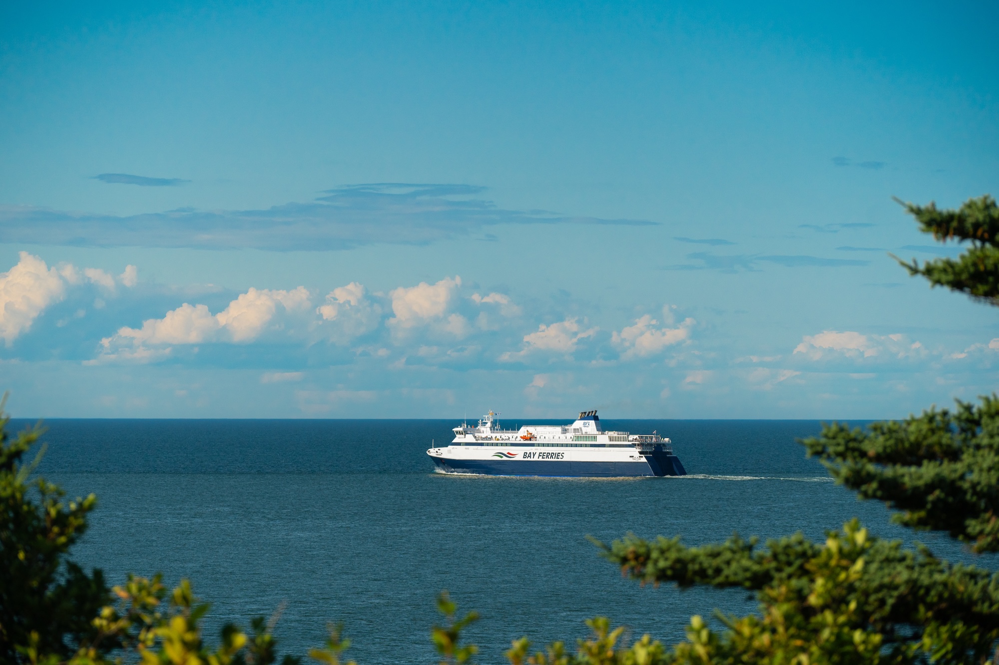 A large ferry sailing in the ocean from a distance on a sunny day, blue skies with a few clouds.