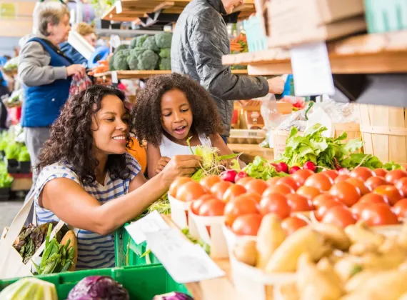 A mother and daughter look at the fresh produce at a market