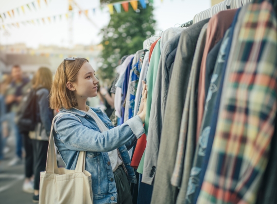 a woman in a jean jacket and white shirt looks through a rack of clothes