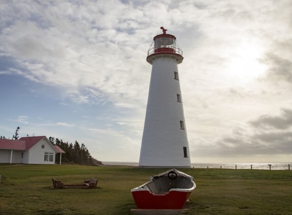 Looking up at a lighthouse on a sunny day, ocean in the background.