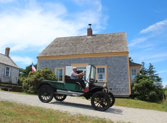 A man drives an old vehicle down a dirt path on a sunny day