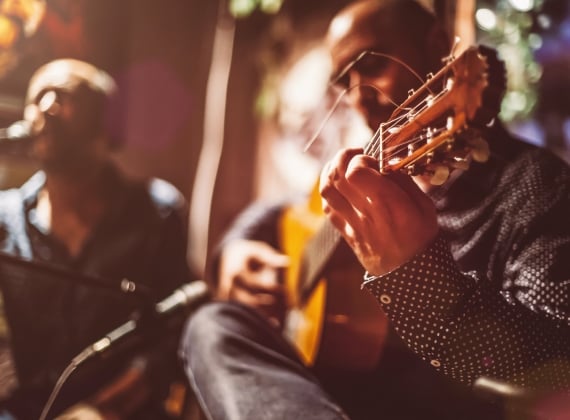 A man playing guitar while another man sings in the background.