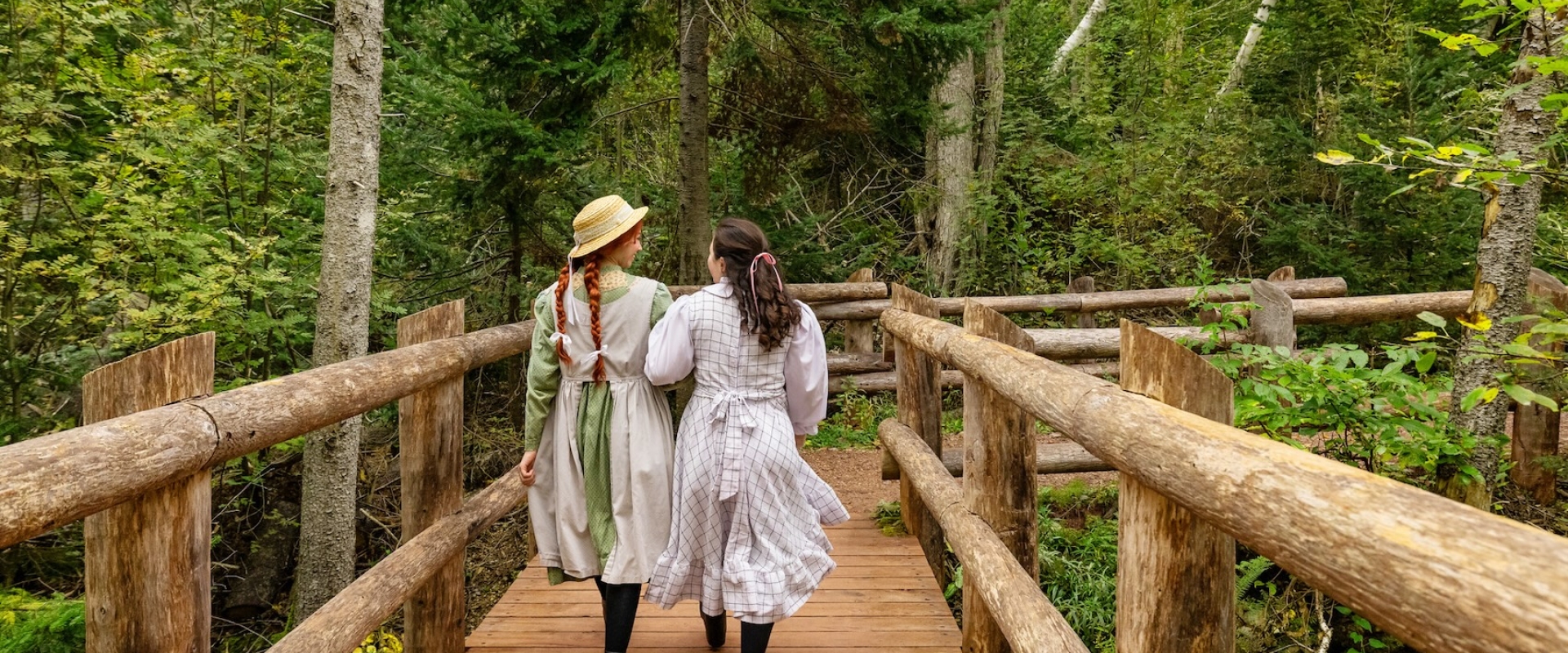 Two girls in traditional clothing walking along the a wooden bridge in PEI National Park