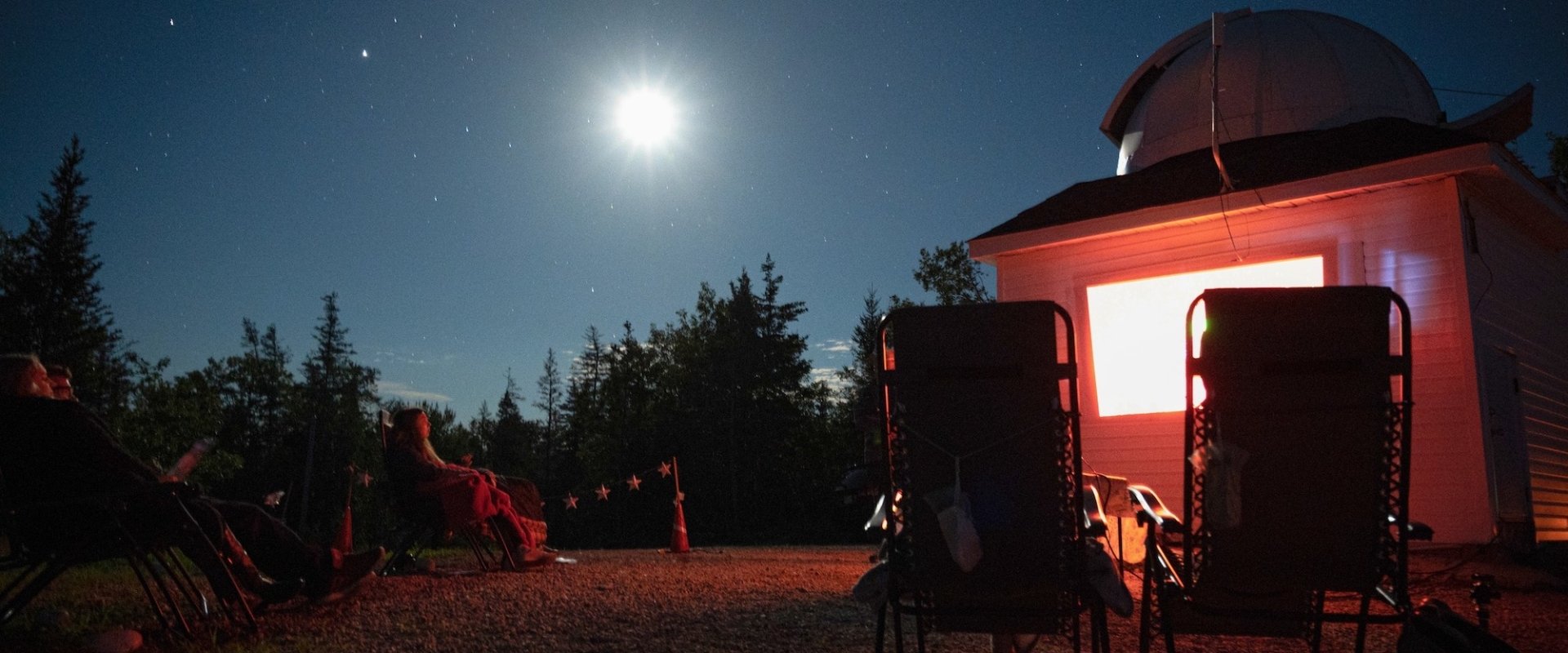 A person sitting outside of a cabin looking at the stars.